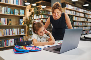 Little student girl doing her homework using laptop in after school club at primary school. teacher