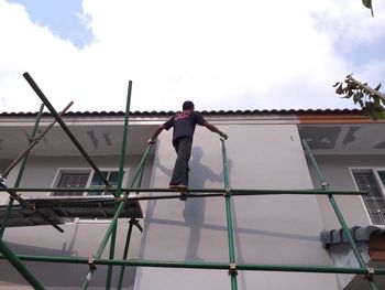 Rear view of man working on building against sky