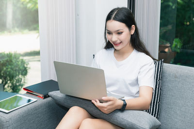 Young woman using mobile phone while sitting in laptop