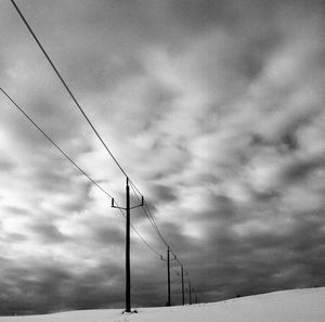 Low angle view of power lines against cloudy sky