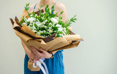 Midsection of woman holding bouquet against white background