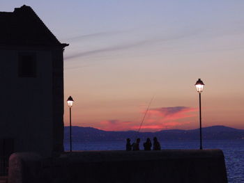 Silhouette people fishing in sea against sky during sunset