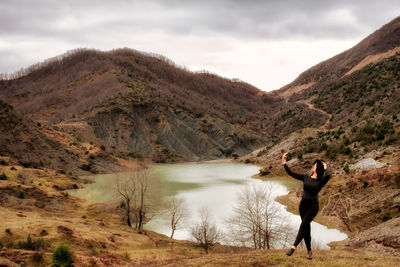 Man standing on mountain by lake against sky