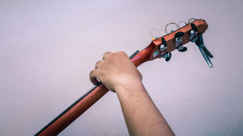 Cropped hand of man holding musical equipment against wall