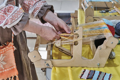 Woman's hands threading colorful warp threads on table loom.