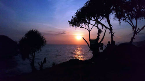 Silhouette trees by sea against sky during sunset