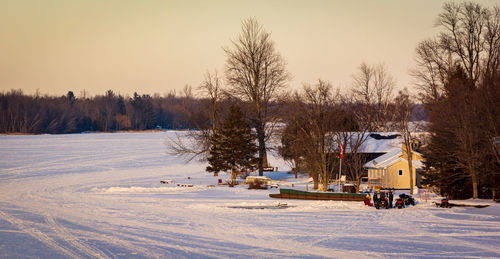 Bare trees on snowy field against sky during sunset