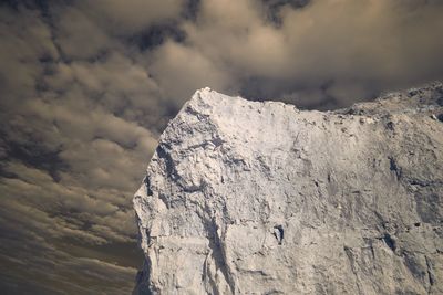 Low angle view of rock formations against cloudy sky during sunny day