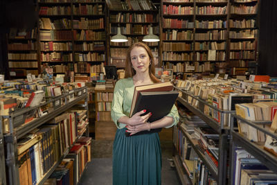 Female student holding books by shelf in library