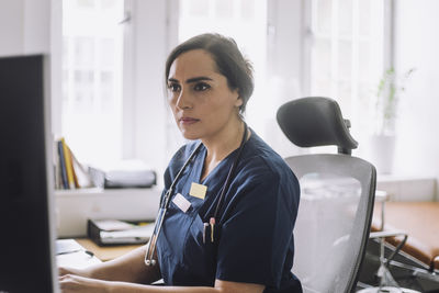 Focused female nurse working while sitting on chair in clinic