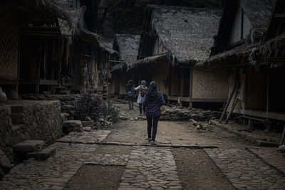 Rear view of people walking on footpath amidst buildings