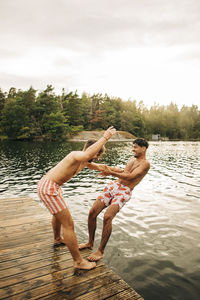 Side view of man at jetty pushing male friend in lake during vacation