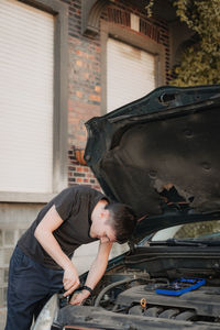 A young man unscrews a car headlight bulb with a screwdriver.