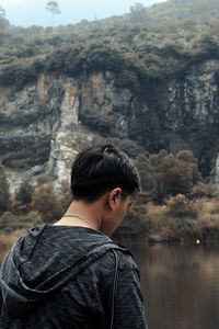Rear view of man standing by lake against mountain