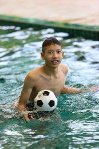 Portrait of shirtless man with ball in swimming pool