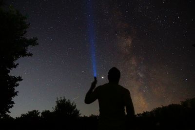 Rear view of silhouette man holding flashlight against sky at night