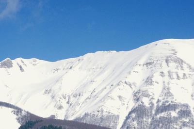 Low angle view of snowcapped mountains against clear blue sky