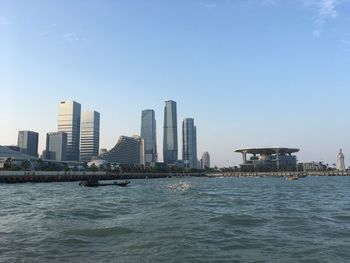 Sea by modern buildings against clear sky