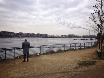 Man looking at river against cloudy sky