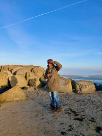 Man standing on rock by sea against sky