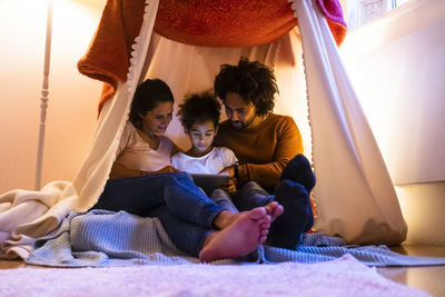 Mother and father using tablet pc with daughter sitting in tent at home