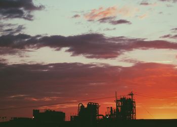 Silhouette factory against cloudy sky at sunset