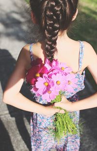 Rear view of girl with flowers standing on road during sunny day