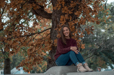Portrait of smiling young woman sitting under tree outdoors
