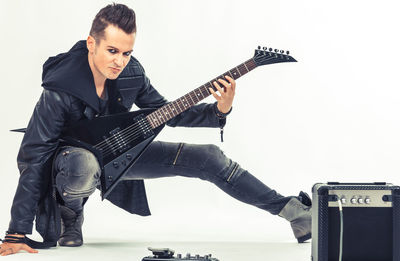 Portrait of young man holding guitar against gray background