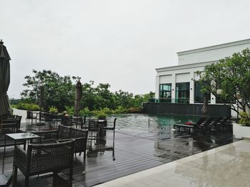 Empty chairs by swimming pool against clear sky