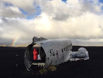 Rear view of woman standing in crashed airplane on field against cloudy sky