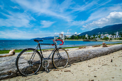 Bicycle parked at beach against cloudy sky