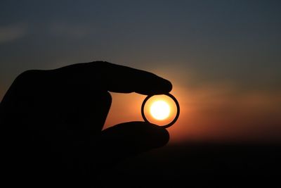 Sun seen through silhouette hand holding ring during sunset