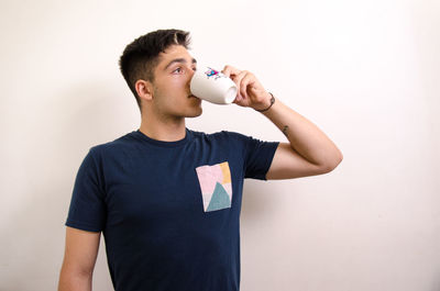 Young man drinking glass against white background