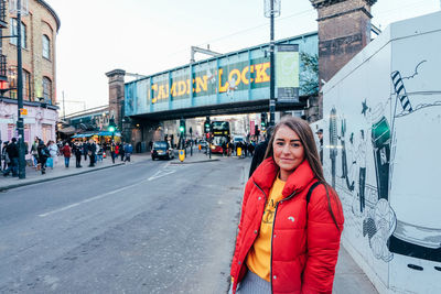 Portrait of young woman standing on sidewalk in city