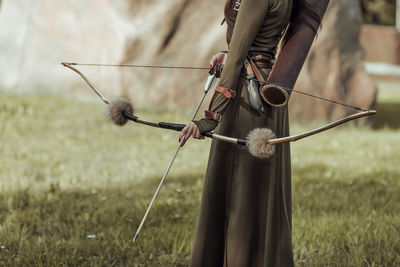 Midsection of archer holding bow and arrow while standing outdoors