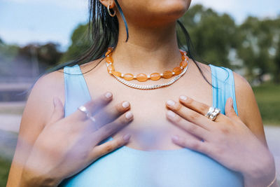 Midsection of woman wearing beaded necklace and chain with hands on chest
