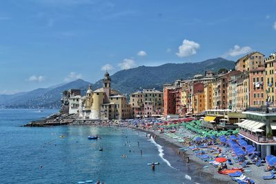 People on sea by buildings in city against sky