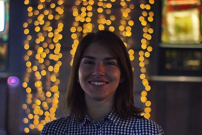 Portrait of smiling woman against illuminated string lights