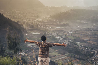 Rear view of man with arms outstretched standing on land