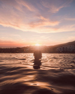 Silhouette man swimming in lake against sky during sunset