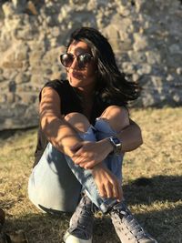 Portrait of young woman wearing sunglasses sitting on land