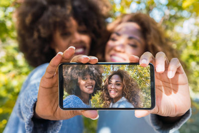 Closeup of afro black friends in a fun mood taking selfie with smartphone using the front camera