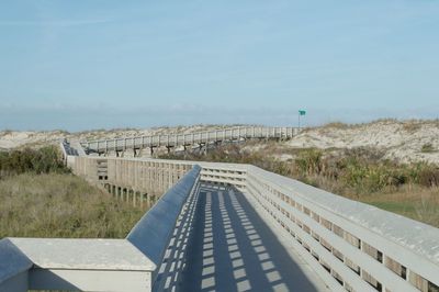 Boardwalk over field against clear blue sky