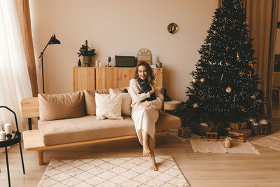Smiling happy girl hugging her pet cat while sitting by a decorated christmas tree in a cozy living