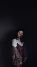 Portrait of smiling young woman standing against black background