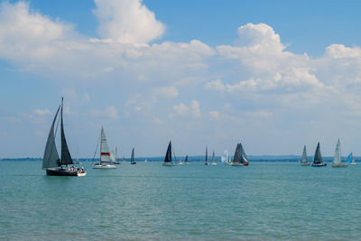 Sailboats sailing in sea against cloudy sky