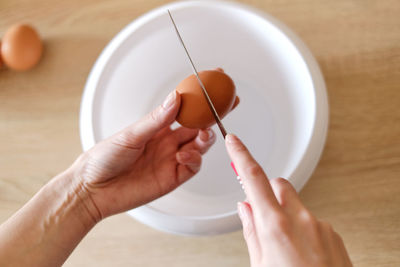 Woman breaks an egg with a knife over a plate to cook a delicious meal