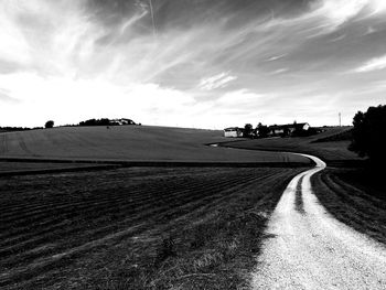 Road by agricultural field against sky