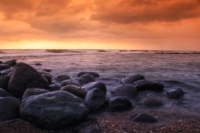 Rocks at beach against sky during sunset